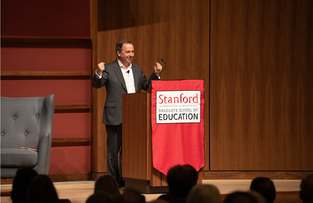 Ron Suskind speaking behind a podium with Stanford GSE logo