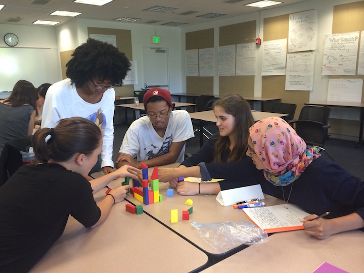 Students gathering around a table assembling a structure using blocks