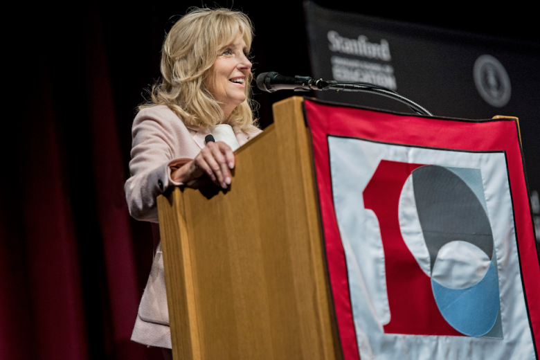 Jill Biden speaking on a podium with Stanford GSE 100 logo