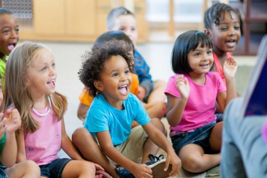 Young school children smiling at the teacher reading.