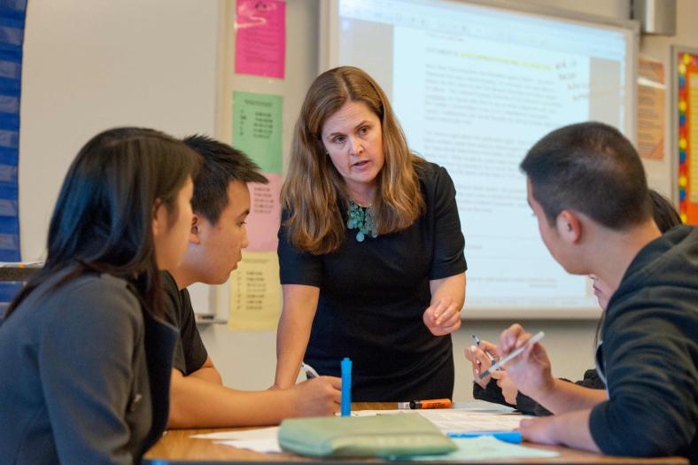 Female teacher speaking with four students at a table.