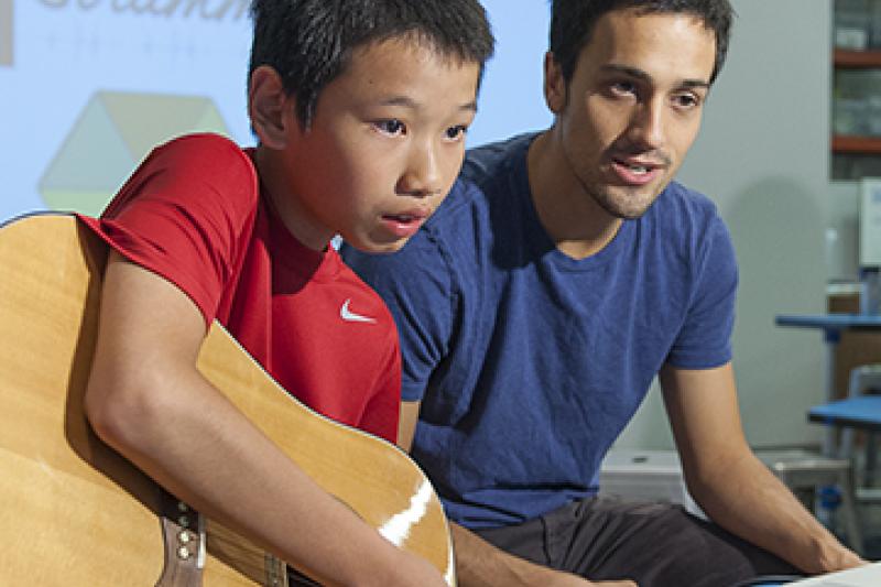 Guitar novice Jim Huang, 12, picks a string as he follows the instructions on the interactive web application called Strummify designed by graduate student Danny Cochran, right. (Photo by L.A. Cicero/Stanford News Service)