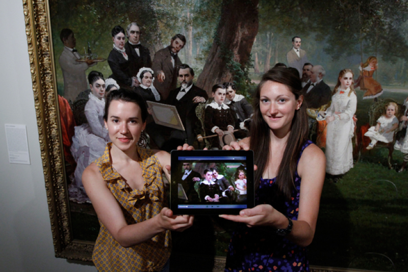 Renee Bruner (left) and Meredith Downing display the app they created as they stand in front of Thomas Hill's painting Palo Alto Spring depicting Leland Stanford Jr's 10th birthday. (Photo: Paul Sakuma)