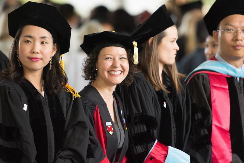 Photo of a female student smiling at a camera in a line of other graduates 