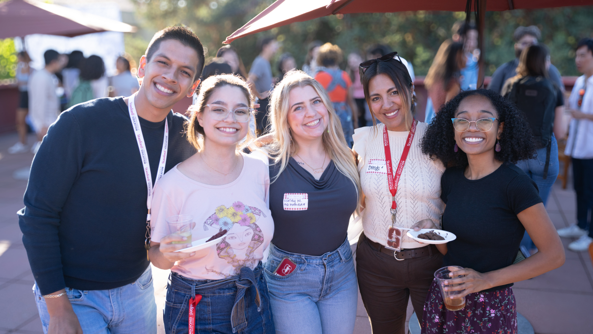 Five new GSE students smiling and holding food and drinks at an outdoor, sunshiny party 