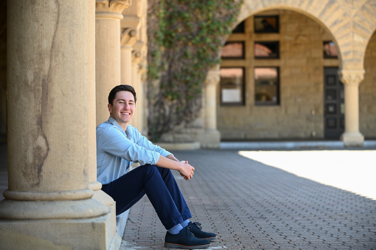 Photo of Ben Thier, sitting by the vine-covered sandstone buildings of Stanford's Main Quad