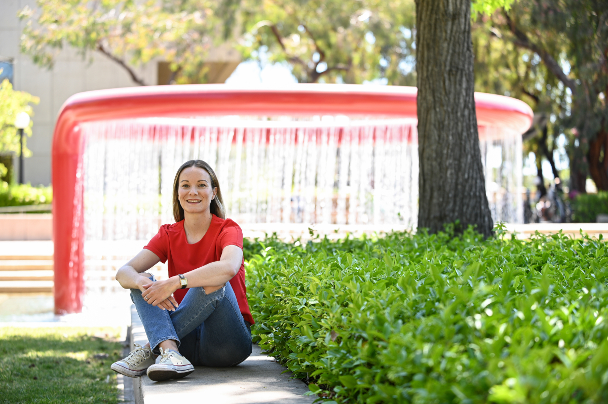 Photo of Jennifer Fortet seated in front of a bright red modern fountain on the Stanford campus