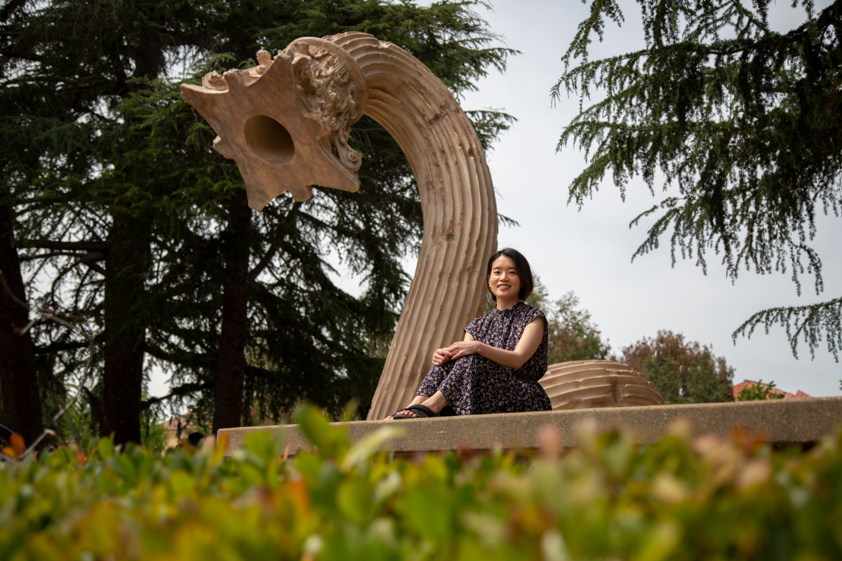 Photo of Risa Ninomiya sitting by a sculpture on the Stanford campus—"Hello," by Xu Zhen