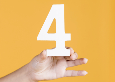 Woman's hand holding up the number 4 against an yellow background