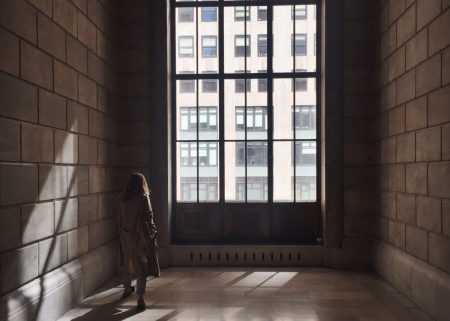 A lone student walks down a dark corridor toward a window