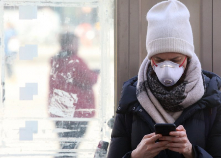 A young woman wearing a mask uses her smartphone