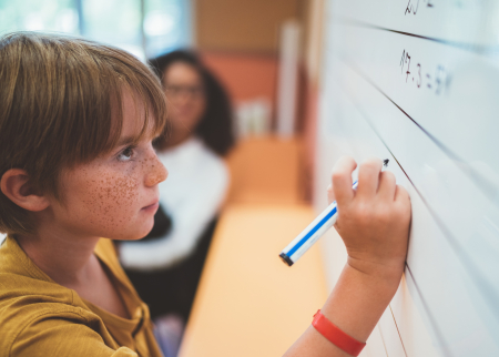 Photo of child doing math problem on a white board