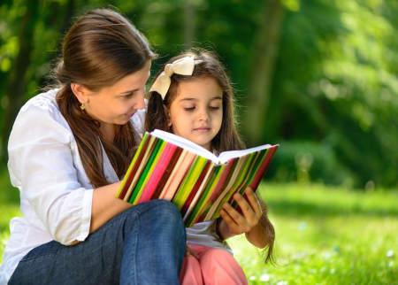Mom is reading a book with her daughter outside 