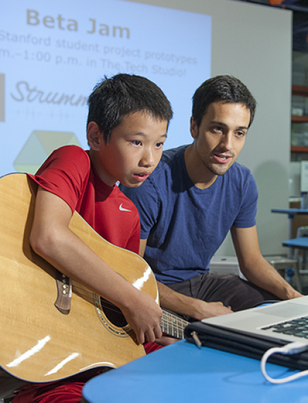 Guitar novice Jim Huang, 12, picks a string as he follows the instructions on the interactive web application called Strummify designed by graduate student Danny Cochran, right. (Photo by L.A. Cicero/Stanford News Service)