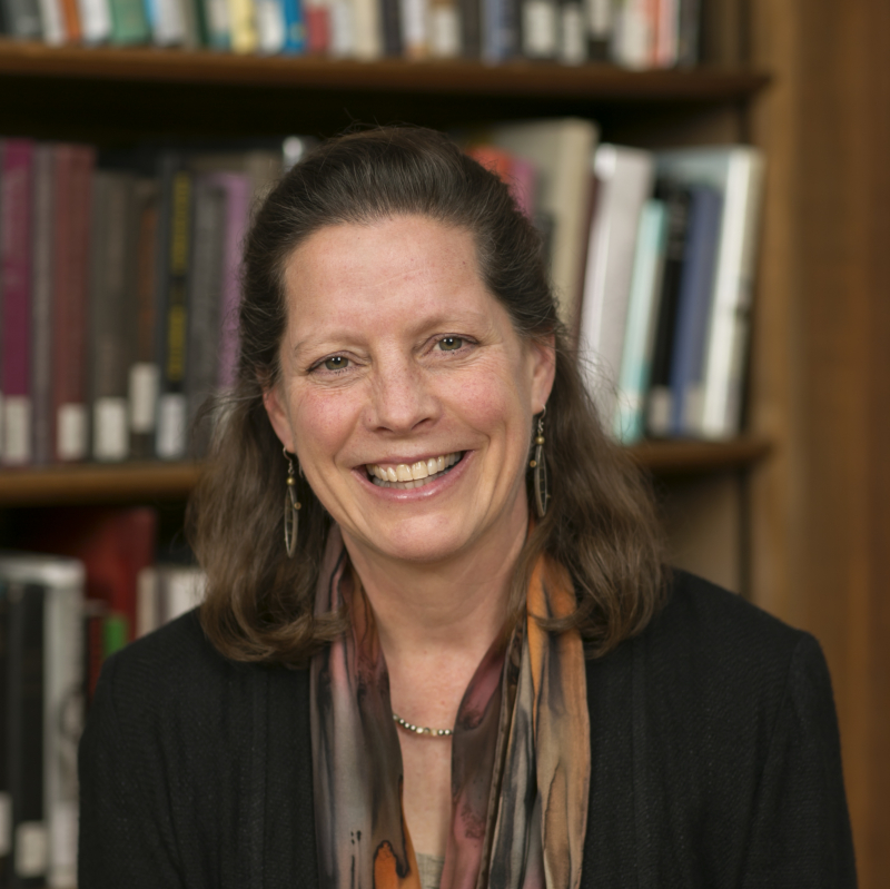 Photo of Alison Cook-Sather, smiling, standing in front of a library book shelf