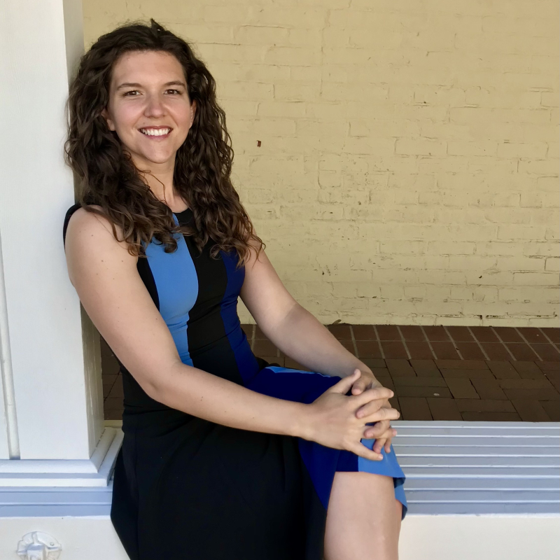 Casual photo of Carrie Townley-Flores, seated, leaning against a pillar in front of a brick wall