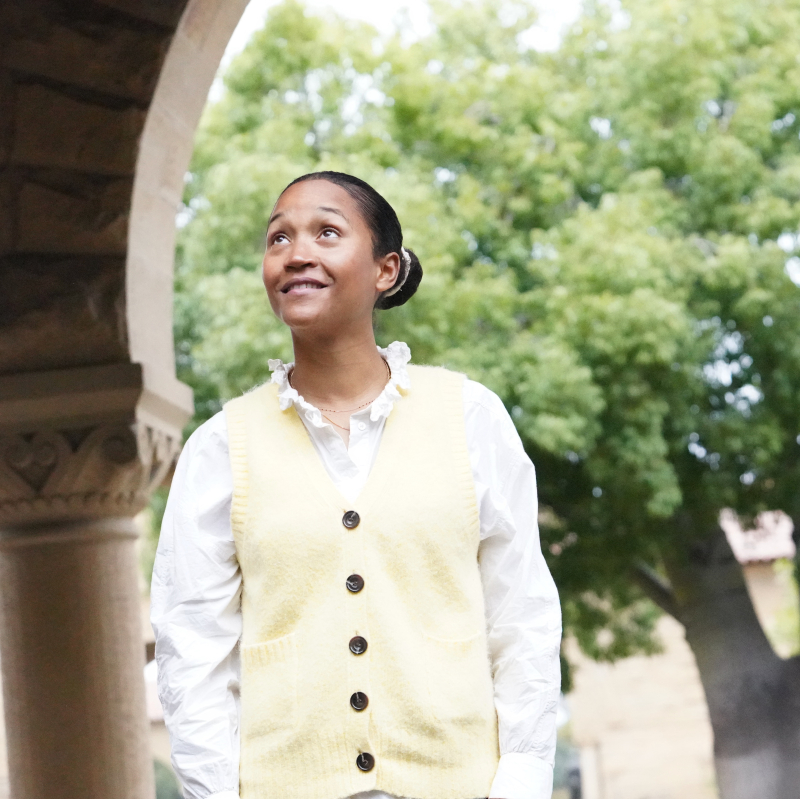 Photo of Camille Fabo, standing in one of the Stanford archways, smiling and looking up