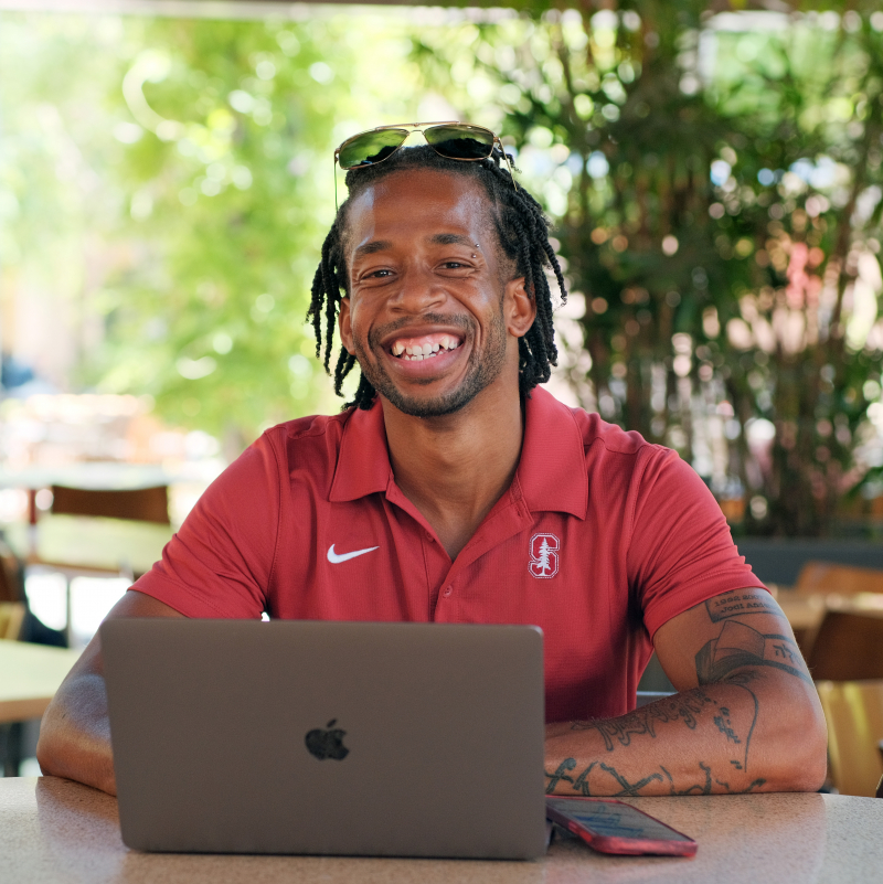 Photo of Jodi Anderson, Jr., smiling, in a cafe with his laptop