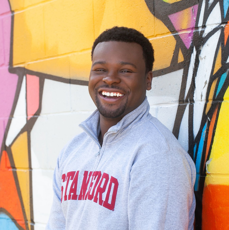 Shyheim Snead, smiling, in front of a colorful wall mural and wearing a Stanford sweatshirt