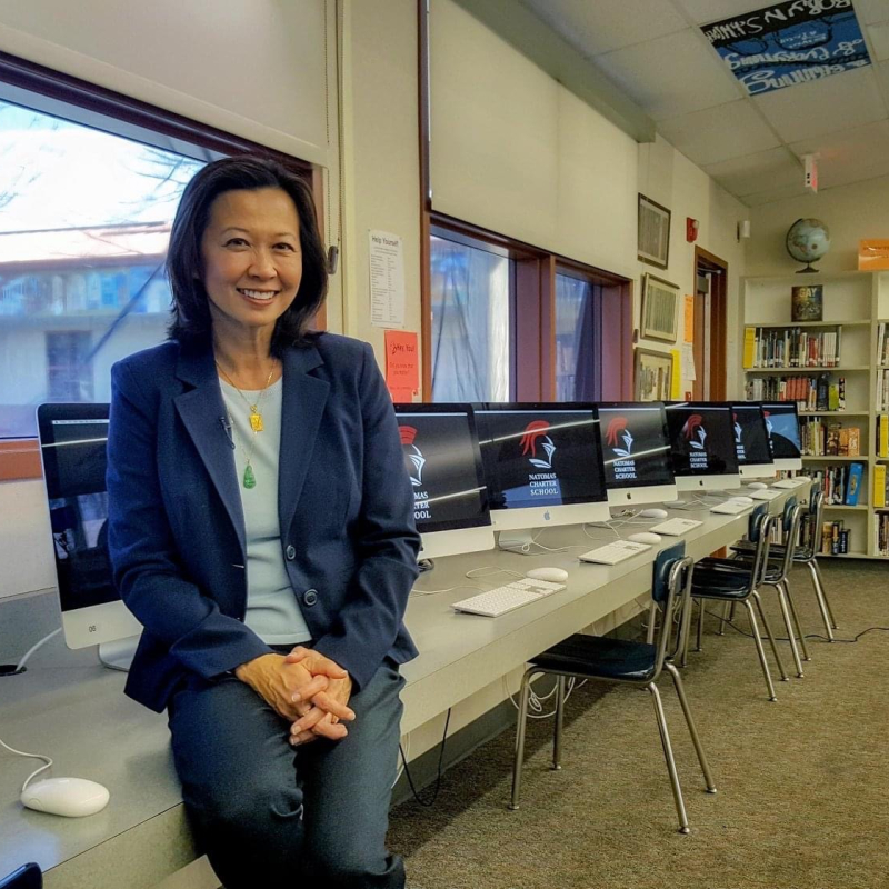 Ting Lan Sun, smiling, in the media center of a school with a row of computers in the background