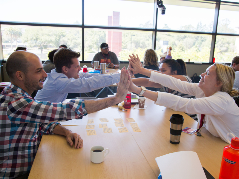 Photo of people around the table give a group high-five
