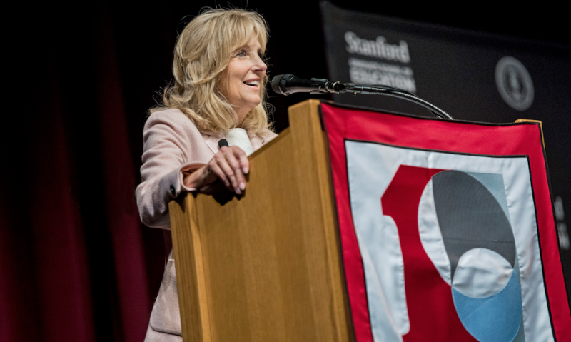 Jill Biden speaking on a podium with Stanford GSE 100 logo