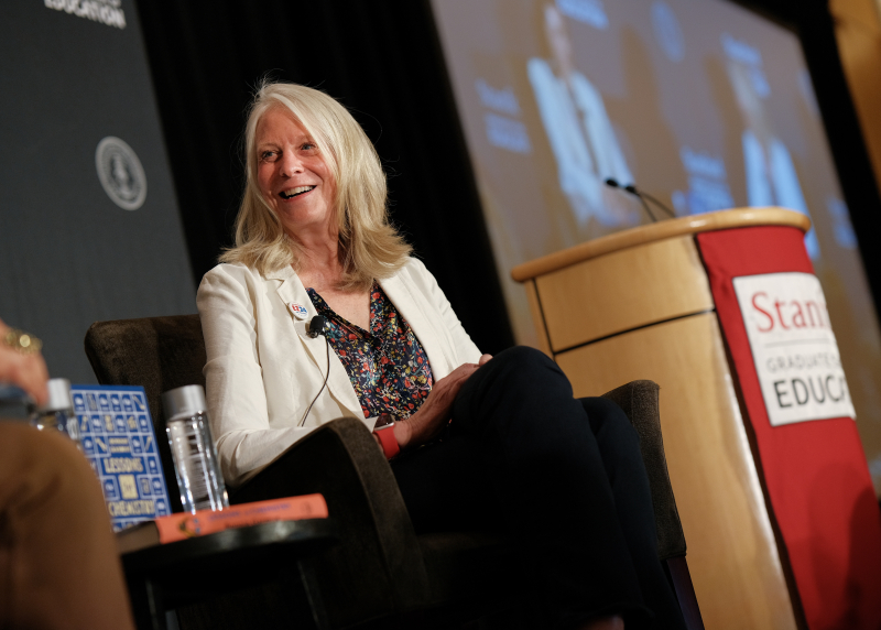 Picture of Bonnie Garmus sitting next to Stanford Graduate School of Education podium