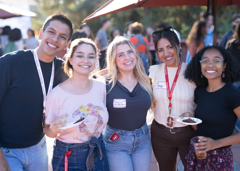 Five new GSE students smiling and holding food and drinks at an outdoor, sunshiny party 