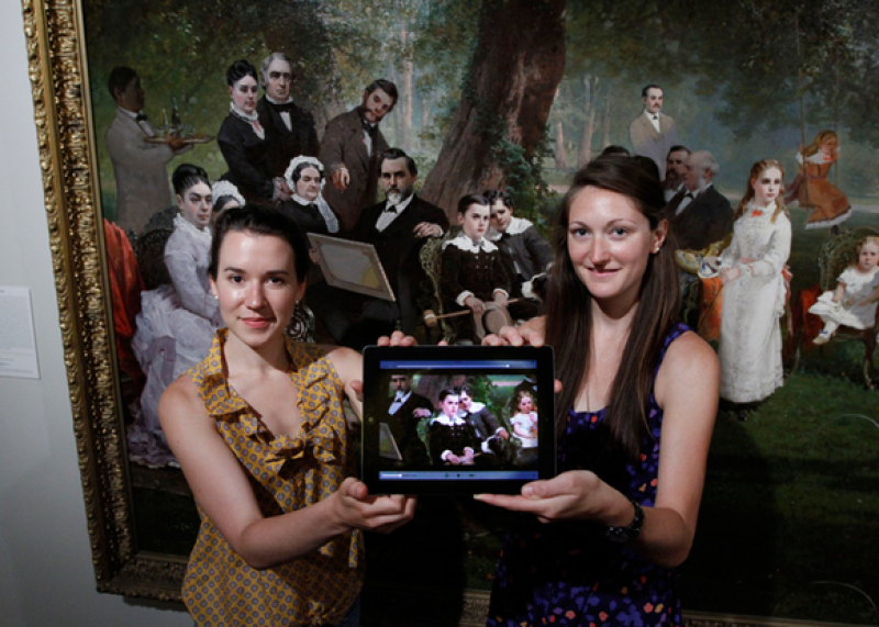 Renee Bruner (left) and Meredith Downing display the app they created as they stand in front of Thomas Hill's painting Palo Alto Spring depicting Leland Stanford Jr's 10th birthday. (Photo: Paul Sakuma)
