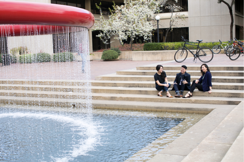 Three students sitting in front of a fountain.