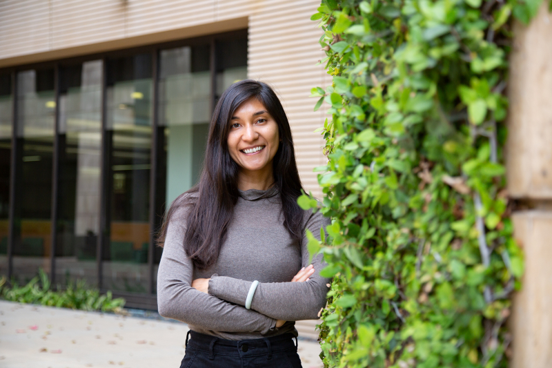 Photo of Abby Li Holst, arms folded and smiling, standing outside a vine-covered building at Stanford