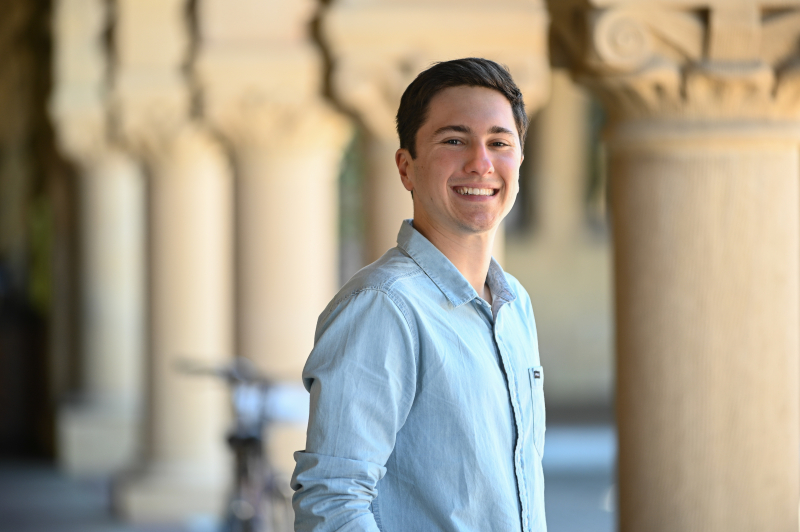 Photo of Ben Thier, smiling, standing near the iconic columns of the Stanford Main Quad