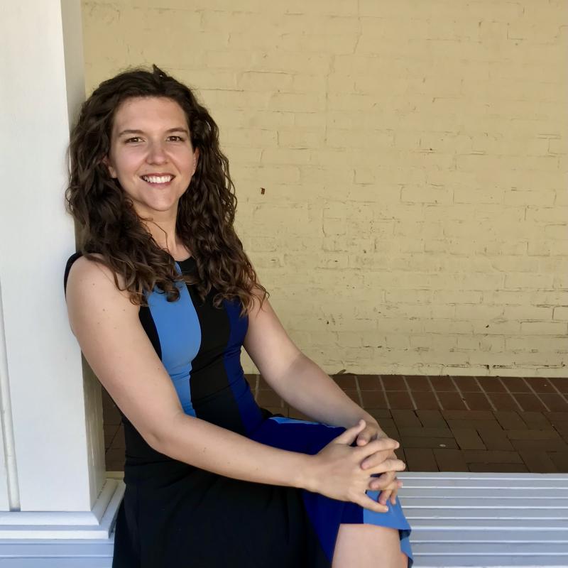 Casual photo of Carrie Townley-Flores, seated, leaning against a pillar in front of a brick wall