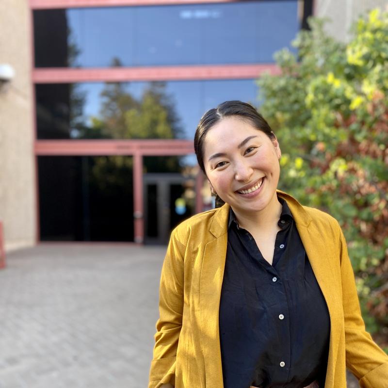 Photo of Facia Desmond at her school, standing near a sign that welcomes students and gives guidance about how to keep others safe during COVID