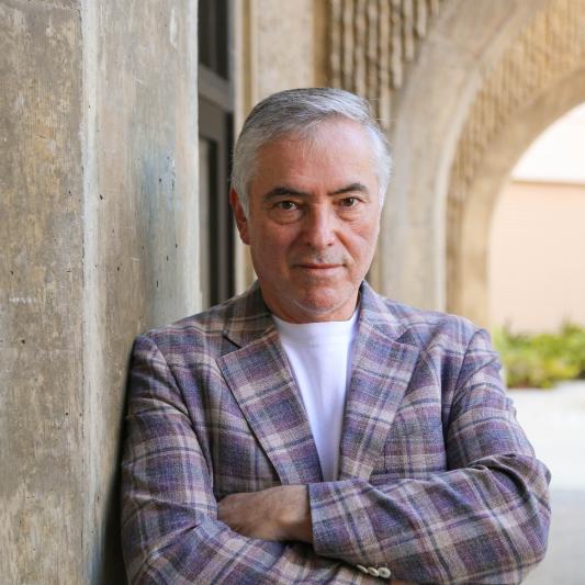 photo of Andre Nudelman, arms folded, in a purple plaid jacket and with Stanford arches behind