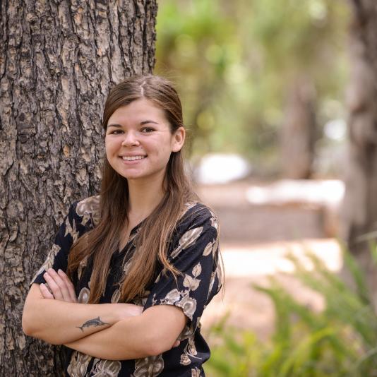 Donya Fegan, standing outside near a tree, arms folded and smiling