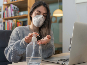 Photo of woman watching video, wearing mask and using hand sanitizer