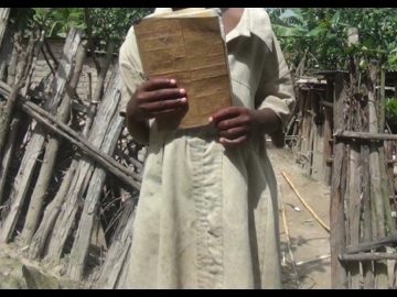 Flora holds the only book she could find in her home. She uses the same book for Kinyarwanda, Maths and English.