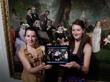 Renee Bruner (left) and Meredith Downing display the app they created as they stand in front of Thomas Hill's painting Palo Alto Spring depicting Leland Stanford Jr's 10th birthday. (Photo: Paul Sakuma)