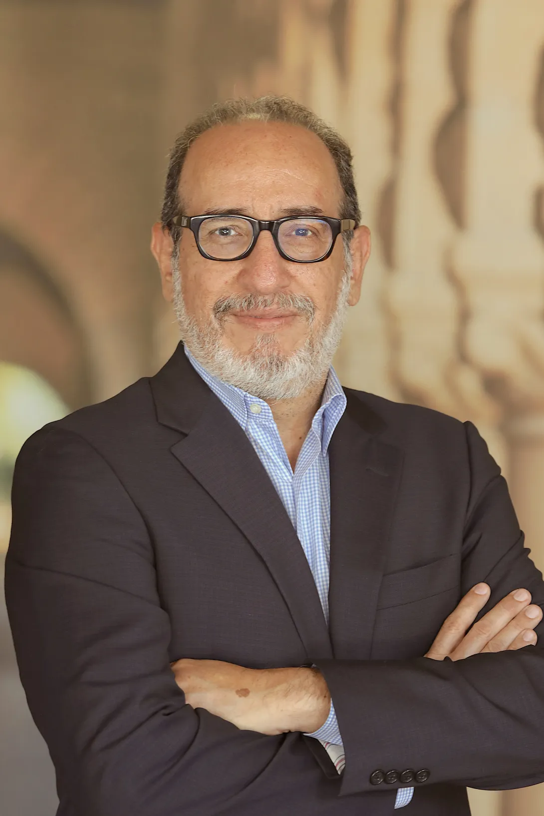 Professor Alfredo J. Artiles, a bearded man wearing glasses, in front of the sandstone arches on the Stanford campus