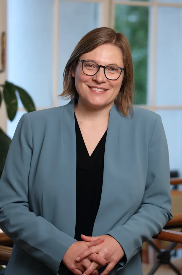 a person with short blonde hair wearing a black shirt, blue cardigan, and glasses