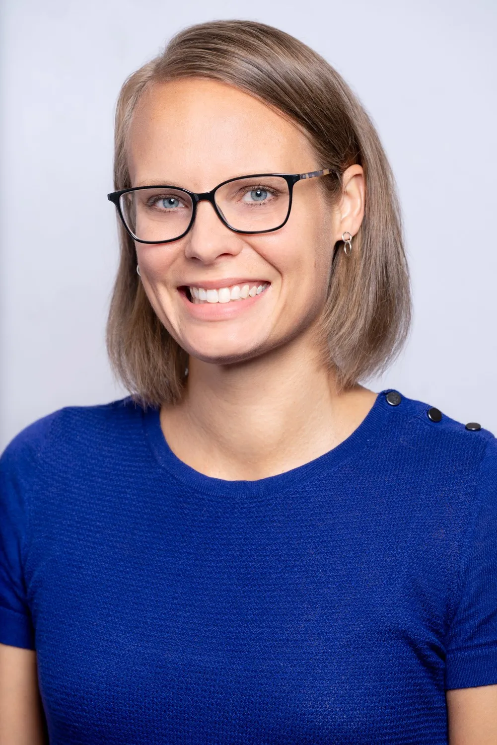 a person with short blonde hair and glasses, wearing a blue shirt