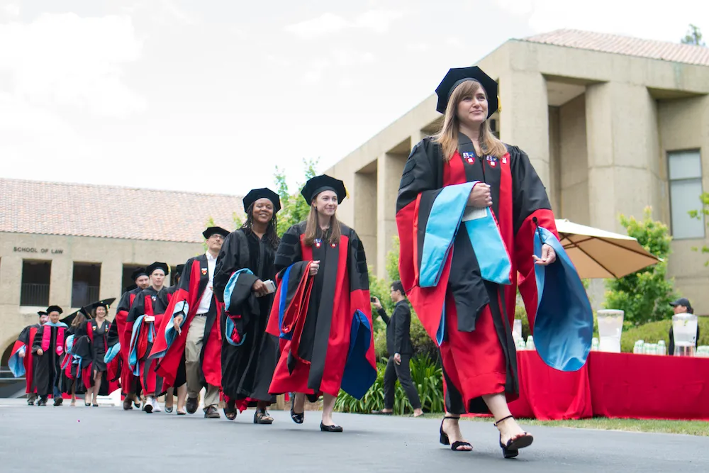 A line of graduating students in robes walking.