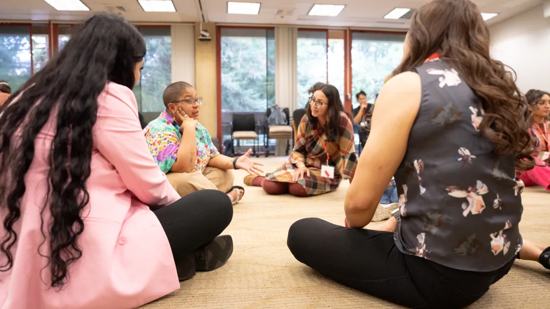 Students sitting in a circle on the floor, in discussion